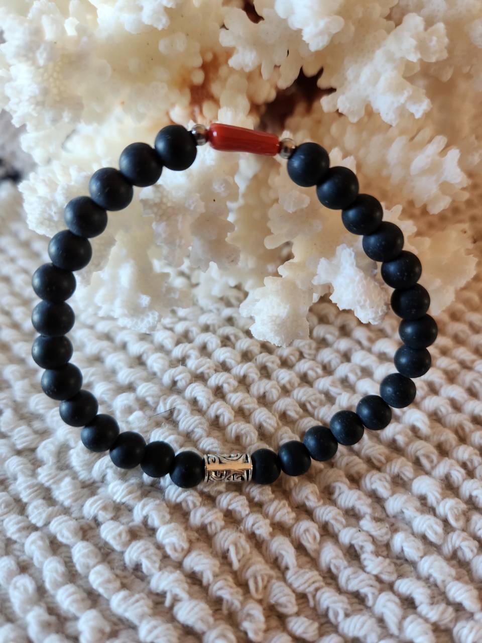 Bracelet pierre naturelle onyx noire avec une perle de corail rouge. Diamètre des perles 6mm Bracelet élastique monté sur du fil cristal très résistant